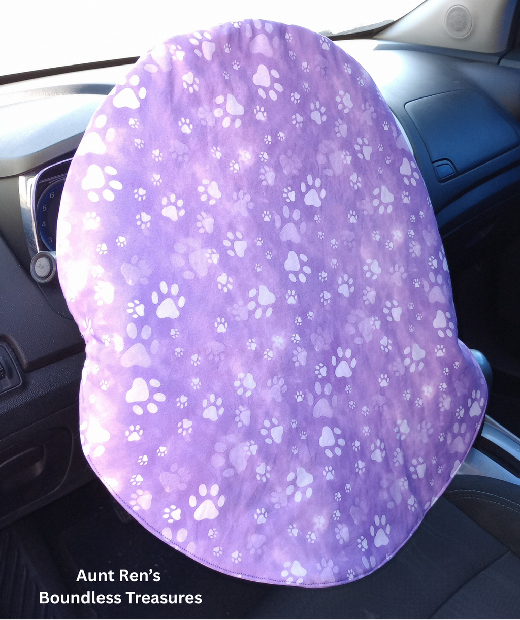 paws on purple fabric slipped over top of car steering wheel