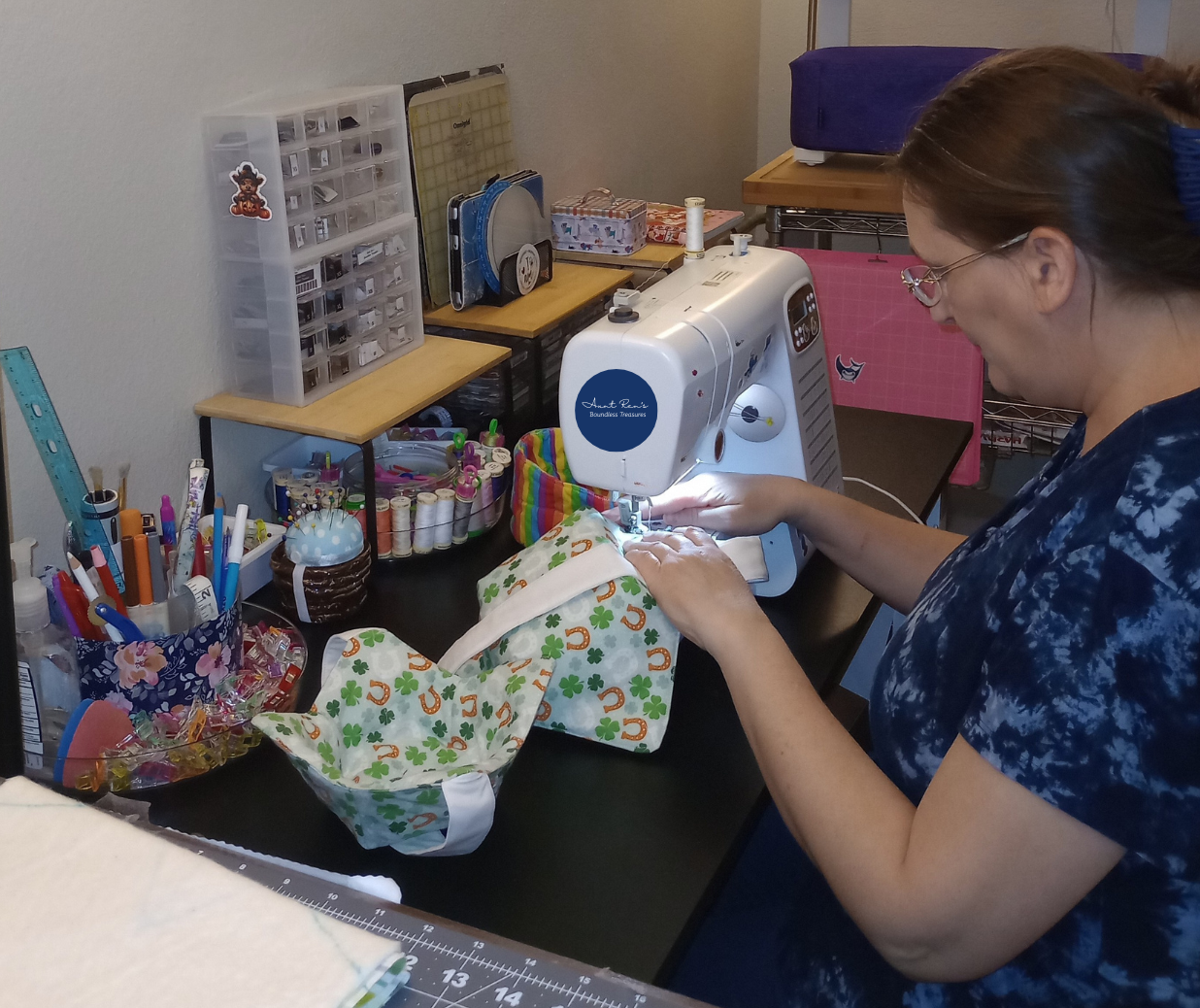 Person using a sewing machine at a table with various items in the background