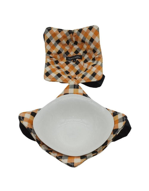 white cotton fabric with orange and black squares reversible bowl cozies with a black versatile strap underneath with a white medium salad bowl resting inside one of the cozies